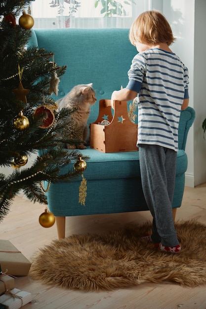 Dziecko i kot domowy dekorują choinkę w piżamie we wnętrzu domu