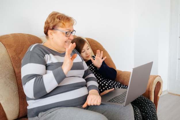 Dziecko i starsza kobieta rozmawiają wideo na swoim laptopie, siedząc na kanapie w domu