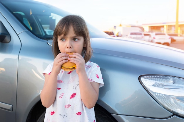 Dziecko je burgera z serem w pobliżu samochodu na świeżym powietrzu