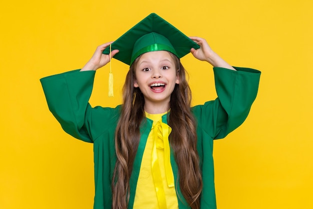 Dziecko jest absolwentem Mała dziewczynka w kapeluszu absolwenta na żółtym, odosobnionym tle Szczęśliwe ukończenie szkoły dla małej dziewczynki Ukończenie szkoły podstawowej