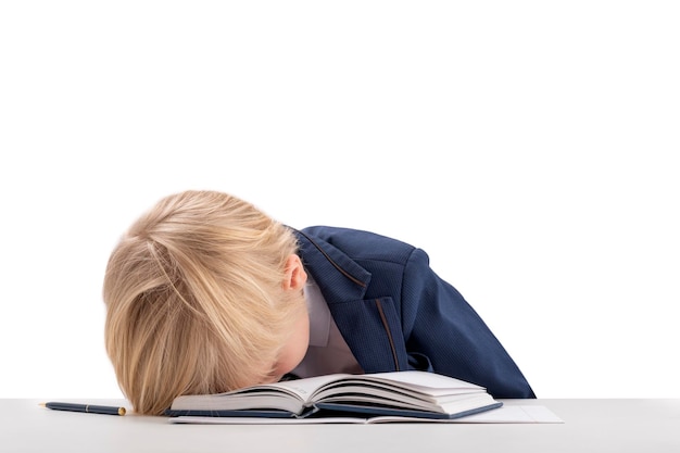 Dziecko jest zmęczone nauką Chłopiec w mundurku szkolnym położył głowę na książce Portret znudzonego ucznia na białym tle