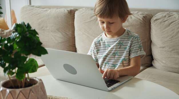 Dziecko korzystające z laptopa siedzącego na kanapie w domu Nauka w domu Nauczanie na odległość