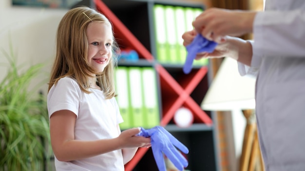 Dziecko lekarz i dziewczynka zakładają rękawiczki medyczne w klinice koncepcja pediatry dla dzieci
