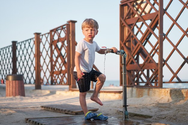 Dziecko Myć Nogi Po Piasku Plaży Kaukaski Chłopiec Stojący Na Plaży. Lato W Dzieciństwie. Urlop Rodzinny Z Jednym Dzieckiem.