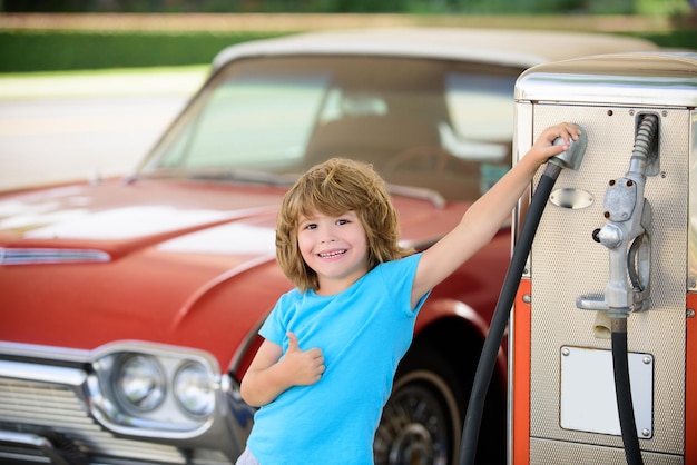 Dziecko na stacji benzynowej przed czerwonym samochodem retro
