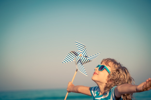dziecko na tle błękitnego morza i nieba trzymające wiatraczek na letnie wakacje