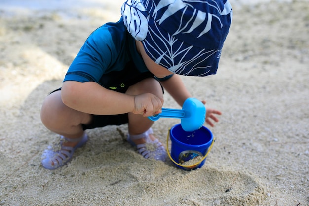 Dziecko na wakacjach na plaży zbierające piasek w wiadrze