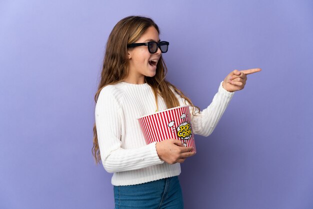 Dziecko nad odosobnioną fioletową ścianą z okularami 3d i trzymając duże wiadro popcorns, wskazując dalej