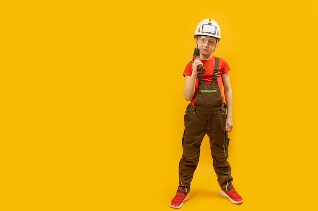 Dziecko nosi kask ochronny i trzyma wiertło w dłoni Chłopiec jako pracownik na żółtym tle Makieta miejsca kopiowania
