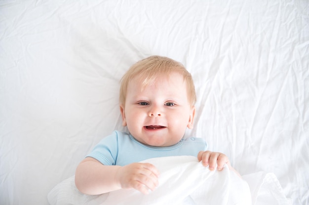 Dziecko o blond włosach uśmiecha się leżąc na białym łóżku widok z góry