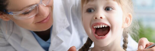 Dziecko odwiedzające lekarza rodzinnego pediatrę z narzędziem sprawdzającym gardło dziewczyna szeroko otwartymi ustami