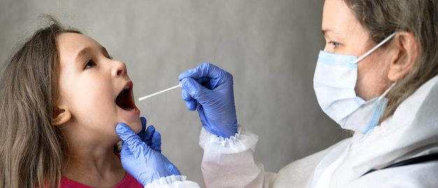 Zdjęcie dziecko otwiera usta do testu pcr covid19, lekarz trzyma wymaz z próbki śliny od małej dziewczynki