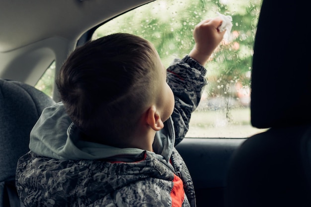 Dziecko pasażera na tylnym siedzeniu samochodu wygląda przez okno samochodu i wyciera szybę serwetką