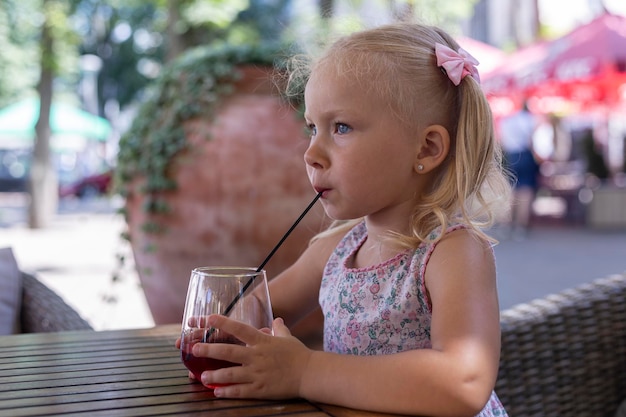 Dziecko pije napój na letnim tarasie w naturalnym świetle. Prawdziwi ludzie.