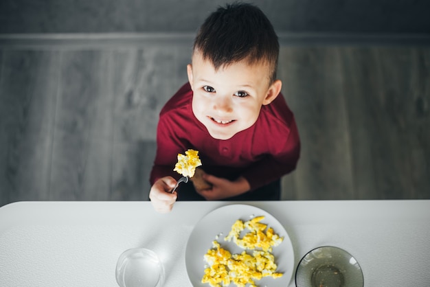 Dziecko Po Południu W Białej Kuchni W Bordowym Swetrze Zjada Omlet