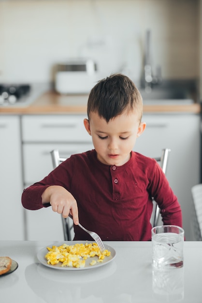 Dziecko Po Południu W Białej Kuchni W Bordowym Swetrze Zjada Omlet