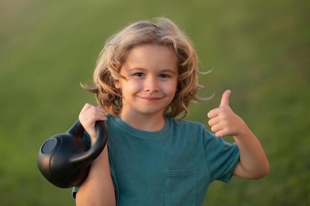 Dziecko podnoszące kettlebell w parku na zewnątrz Chłopiec pracujący z hantlami Sport dla dzieci i aktywne zdrowe życie Sport i szkolenia dla dzieci