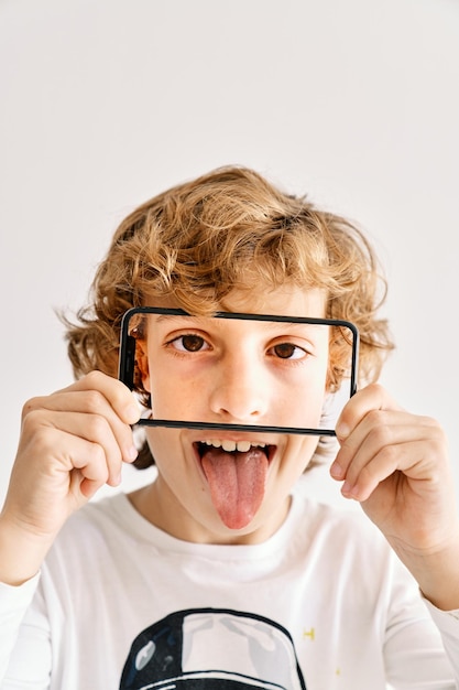 Zdjęcie dziecko pozujące z telefonem komórkowym i zdjęciami części jego twarzy