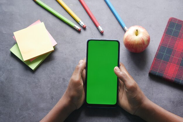 Dziecko ręka trzyma inteligentny telefon z zielonym ekranem na stole