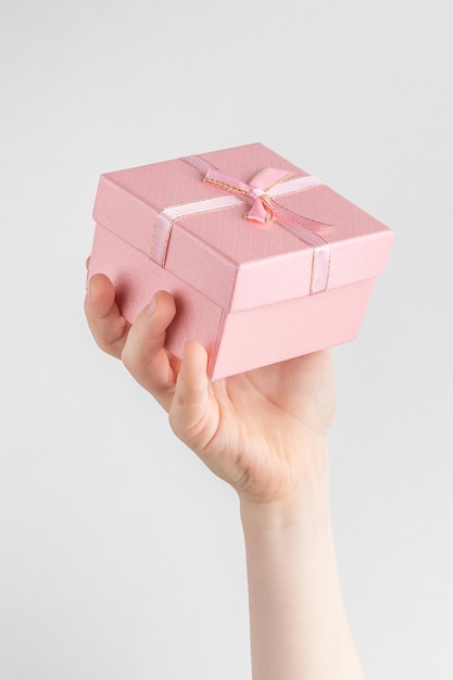 Zdjęcie dziecko ręka trzyma pudełko z różową kokardką białe i szare tło z miejscem na kopię