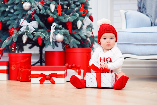 Dziecko rozpakowywa prezentów pudełka z boże narodzenie dekoracją, ubierającą jako Santa, bokeh zaświeca, zima wakacje pojęcie