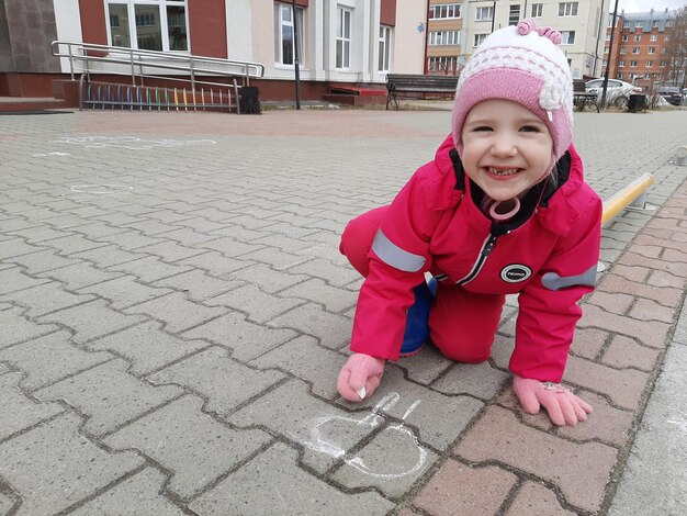 Zdjęcie dziecko rysuje na ziemi, czteroletnia dziewczyna rysuje na ulicy.