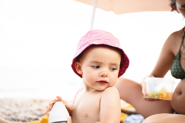 Dziecko siedzące na plaży obok matki pod parasolem