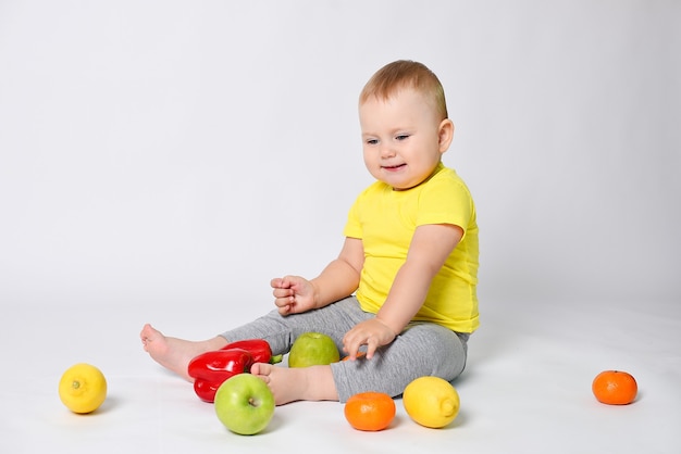 Zdjęcie dziecko siedzi na białym tle w żółtej koszulce z owocami i warzywami