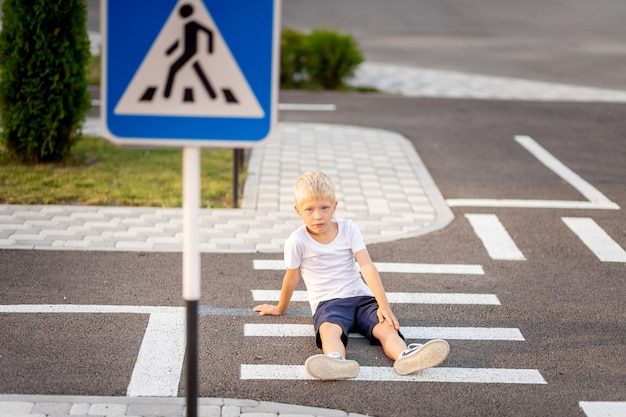 Zdjęcie dziecko siedzi na jezdni na przejściu dla pieszych i trzyma się za nogę
