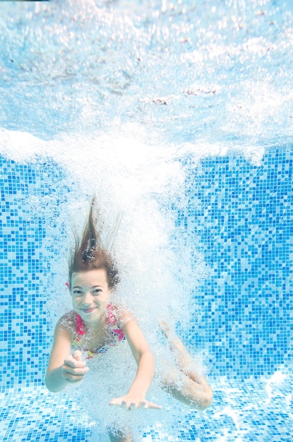 Dziecko skacze do basenu i pływa pod wodą mała aktywna dziewczynka nurkuje i bawi się pod wodą
