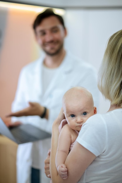 Dziecko sprawdź. Blondynka młoda kobieta z dzieckiem rozmawia z pediatrą w klinice