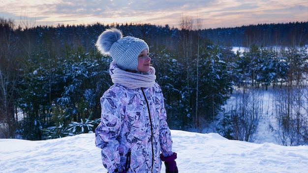 Dziecko stoi na wzgórzu na tle zimowego lasu.