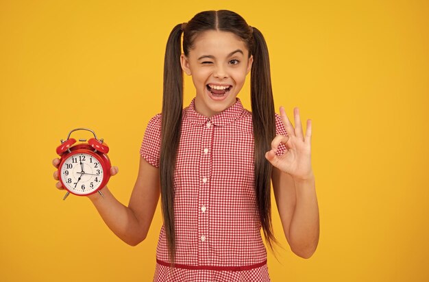 Dziecko studentka z zegarem na żółtym tle Dziecko z powrotem do szkoły Koncepcja edukacji i czasu Szczęśliwa nastolatka pozytywne i uśmiechnięte emocje nastoletniej dziewczyny