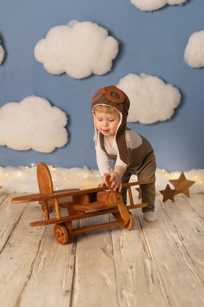 Dziecko to chłopiec w kombinezonie pilota z drewnianym samolotem na tle białych chmur