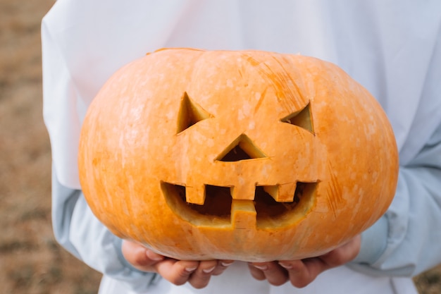 Dziecko ubrane w kostium na Halloween, trzymając rzeźbione dyni.