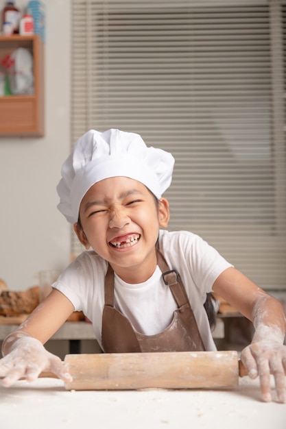 Dziecko w białym kapeluszu szefa kuchni i uśmiechnięte ze szczęścia.