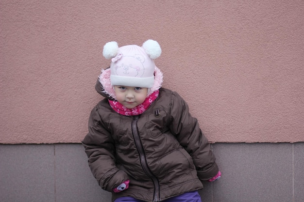 Dziecko w ciepłym ubraniu w sezonie zimowym patrzące na aparat stojący w pozie na fioletowym tle