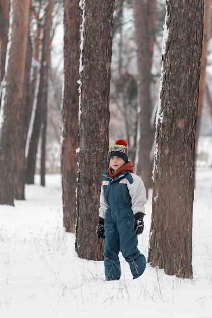 Dziecko w czapce i zimowym kombinezonie spaceruje na tle zimowego lasu Pionowa ramka