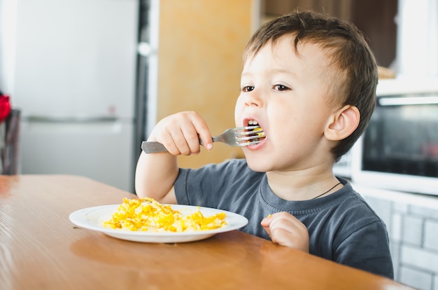 Dziecko w koszulce w kuchni jedzące omlet, rozwidla się