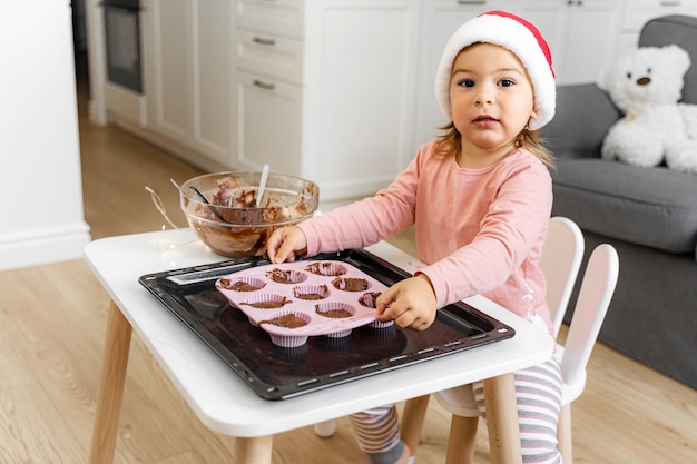 Dziecko w santa hat przygotowuje świąteczne ciasteczka w domu. Świąteczna aktywność w domu dla malucha