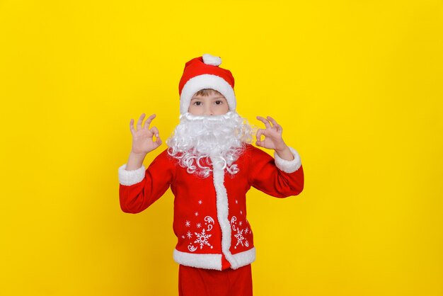 Dziecko w stroju Świętego Mikołaja i ze sztuczną brodą wykonuje gest OK obiema rękami