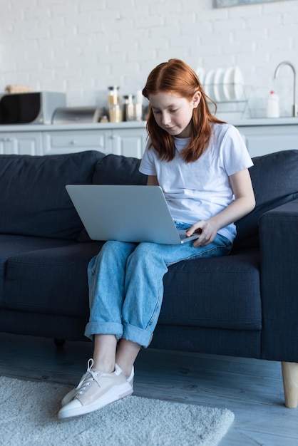 dziecko w wieku przed nastoletnim używające laptopa na kanapie w domu