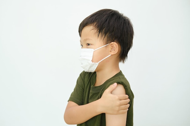 Dziecko w wieku szkolnym po otrzymaniu szczepionki Małe dziecko noszące maskę medyczną pokazującą ramię z bandażem po otrzymaniu szczepionki miało skutki uboczne ból ramienia Szczepionka COVID 19 dla dzieci i młodzieży