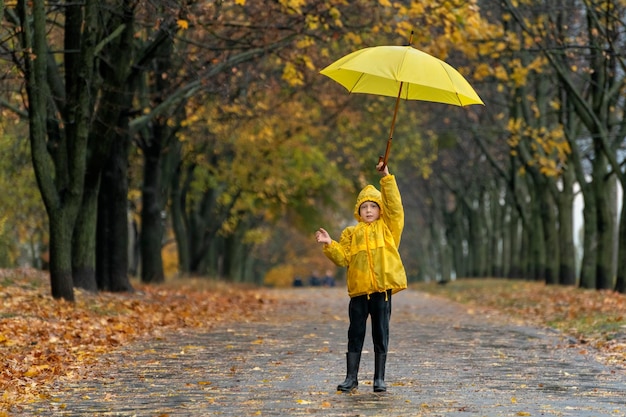Dziecko w żółtym płaszczu przeciwdeszczowym spaceruje po jesiennym parku z dużym żółtym parasolem w dłoniach Deszczowy dzień