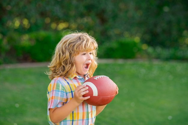 Dziecko z piłką do rugby słodkie dziecko bawiące się i grające w futbol amerykański na zielonej trawie parku