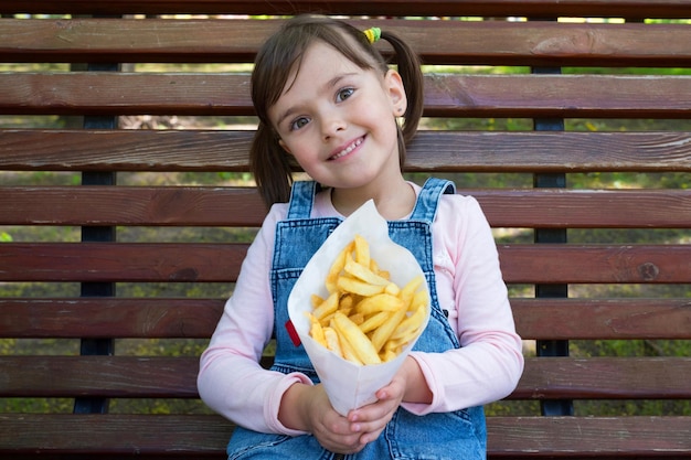Dziecko z uśmiechem siedzi na ławce i trzyma paczkę ziemniaków