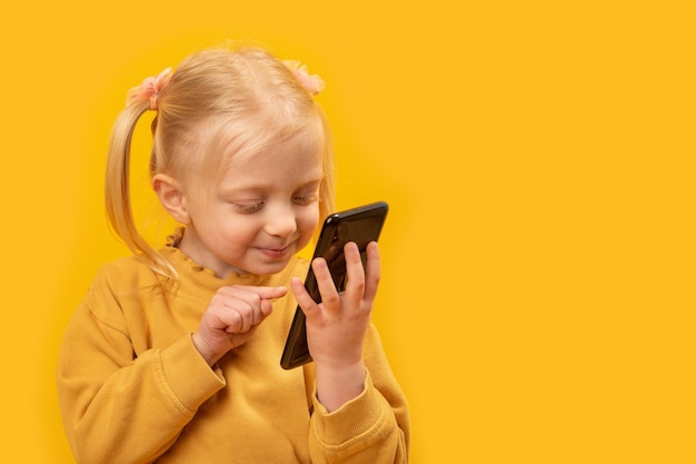 Zdjęcie dziecko ze smartfonem w rękach mała dziewczynka przewijanie paszy na smartfonie lub gra w grze żółtym tle