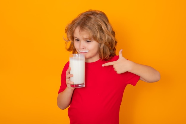 Dziecko ze szklanką mleka na tle studia Ładny chłopiec w białej koszuli trzymający szklankę mleka na odizolowanym na żółto Portret dziecka z mlecznymi wąsami