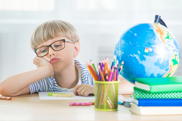 Dziecko zmęczone nauką. Niezadowolony student Wyczerpany mały uczeń. Chłopiec w klasie. Dziecko odrabiania lekcji.