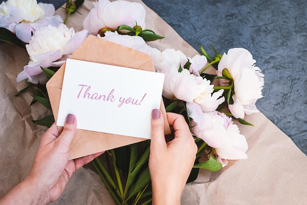 Dziękuję karta w rękach wiadomość koperta różowy bukiet kwiatów piwonii